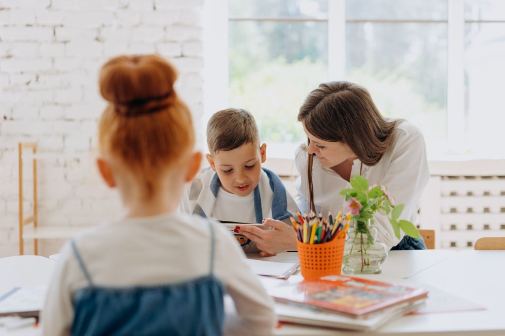 a-pontoise-l-inclusion-scolaire-face-au-manque-de-moyens-2 Une enseignante se penche vers un garçon assis à une table, tandis qu’une fille est au premier plan dans une classe