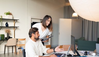Un homme en fauteuil roulant travaille sur un ordinateur, accompagné d’une collègue dans un bureau