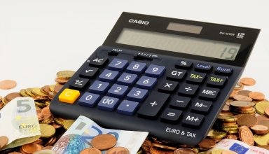 Calculatrice posée sur des billets de 5 et 20 euros entourés de pièces de monnaie