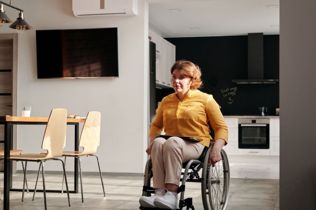 14-innovations-pour-renforcer-autonomie-et-accessibilite-au-quotidien Femme en fauteuil roulant dans une cuisine ouverte, près d’une table et de chaises