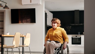 Femme en fauteuil roulant dans une cuisine ouverte, près d’une table et de chaises