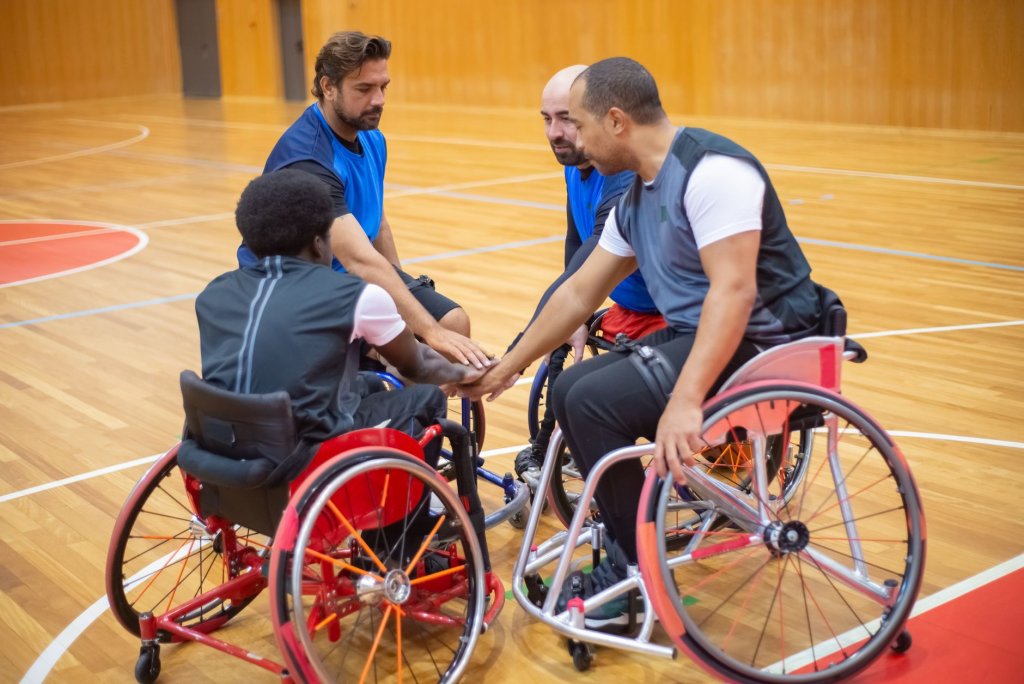 l-equipe-paralympique-vietnamienne-installee-au-japon Quatre joueurs de basket en fauteuil roulant se rassemblent, mains jointes, sur un terrain intérieur